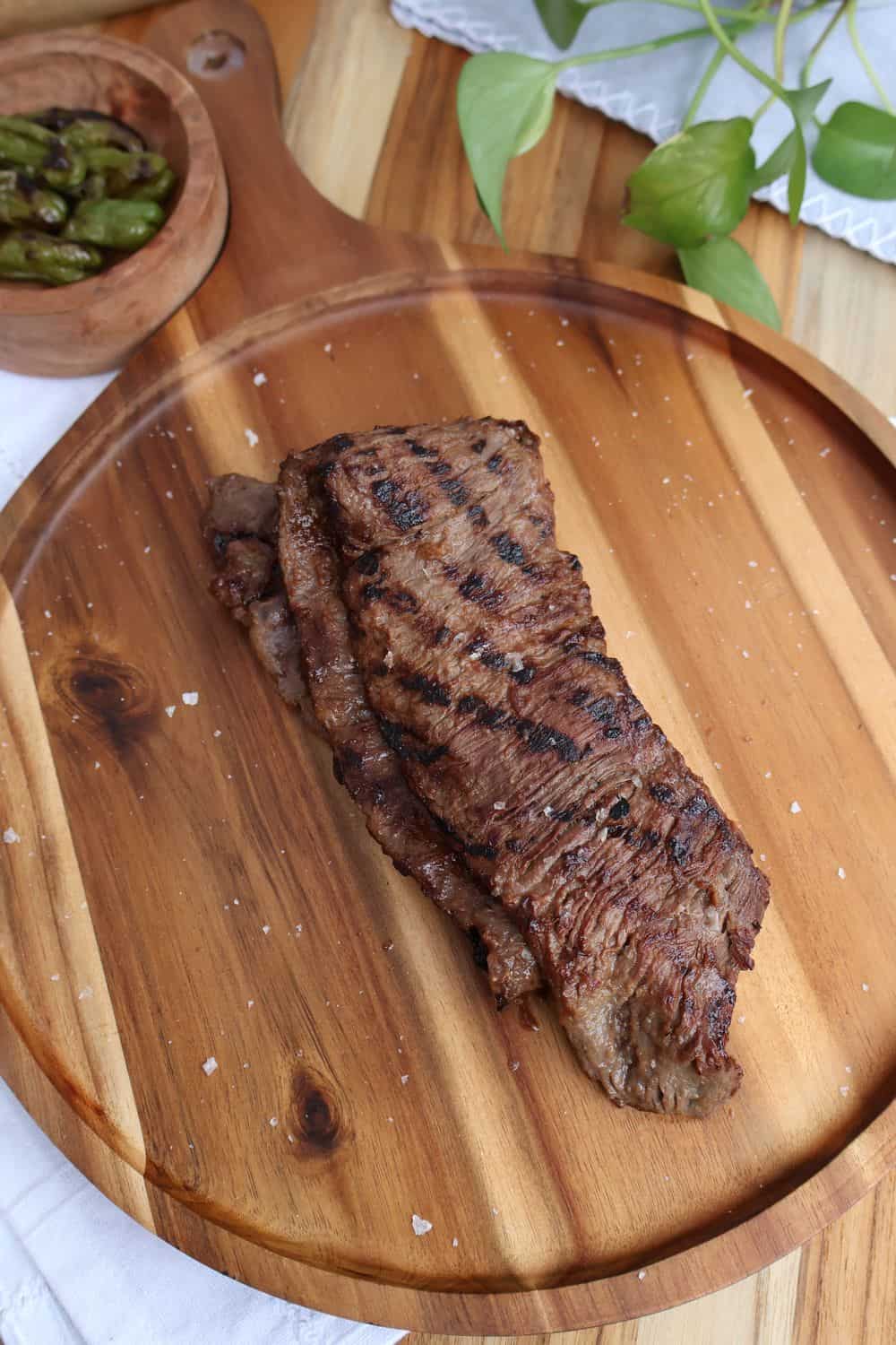 Grilled wagyu skirt steak on a wood board with charred shishitos and fresh basil