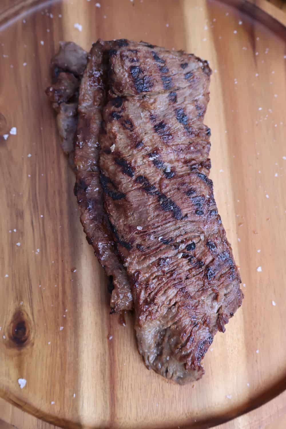 Sliced wagyu skirt steak on a wood board, thin against-the-grain slices with charred edges and flaky sea salt