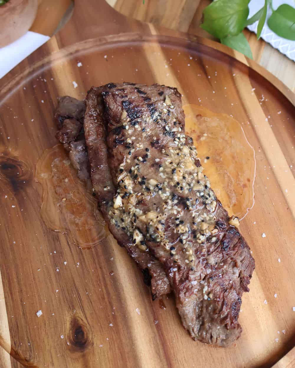 Grilled wagyu skirt steak resting on a wood board with sesame butter melting on top