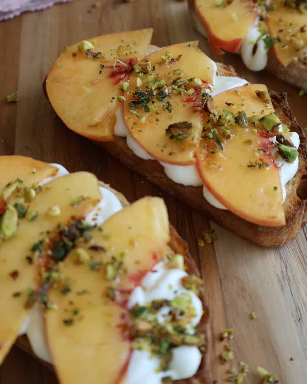 Assembled peach bruschetta with whipped ricotta and chopped pistachios on a wooden board