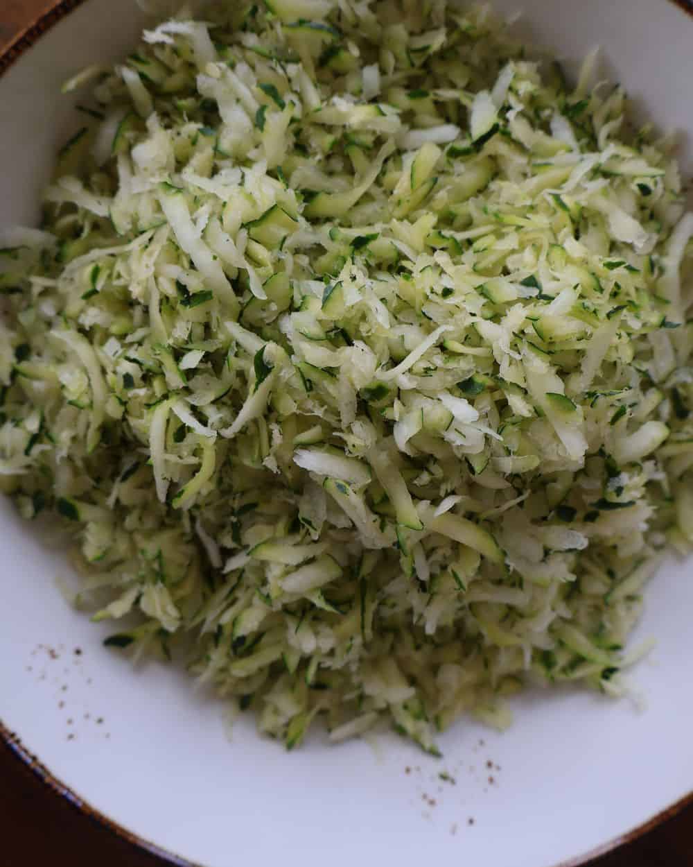 Grated zucchini, well drained, in a white bowl