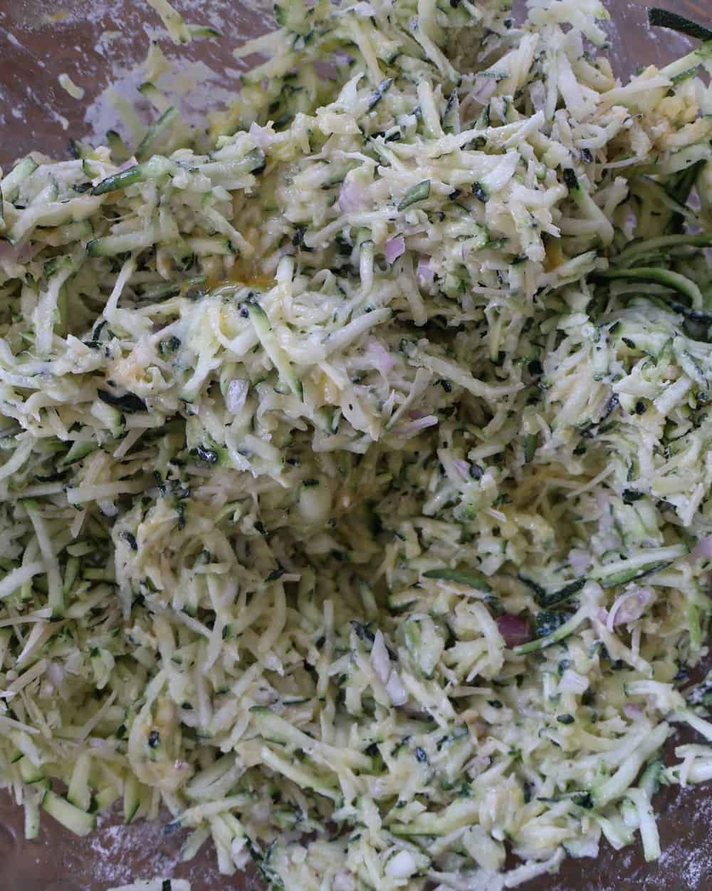 Zucchini fritter batter mixed with shallot and parmesan in a glass bowl