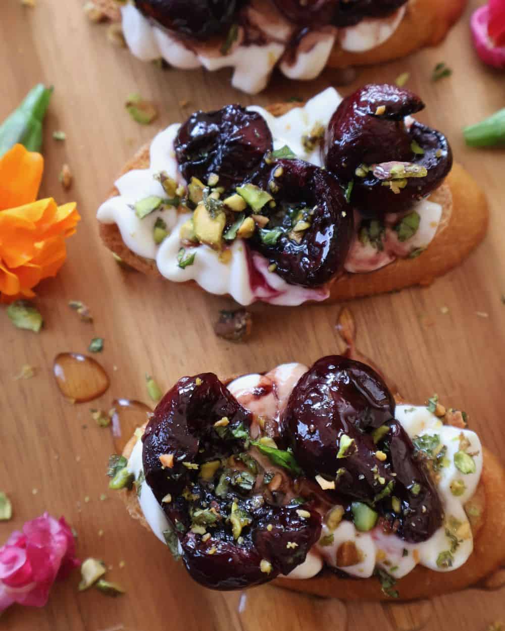 Assembled cherry bruschetta topped with pistachio mint crumble on a wood board