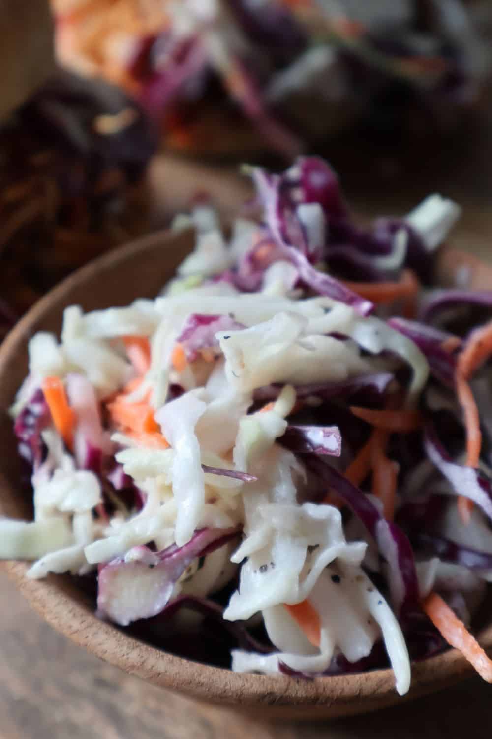 Creamy coleslaw in a small wooden bowl beside pulled pork