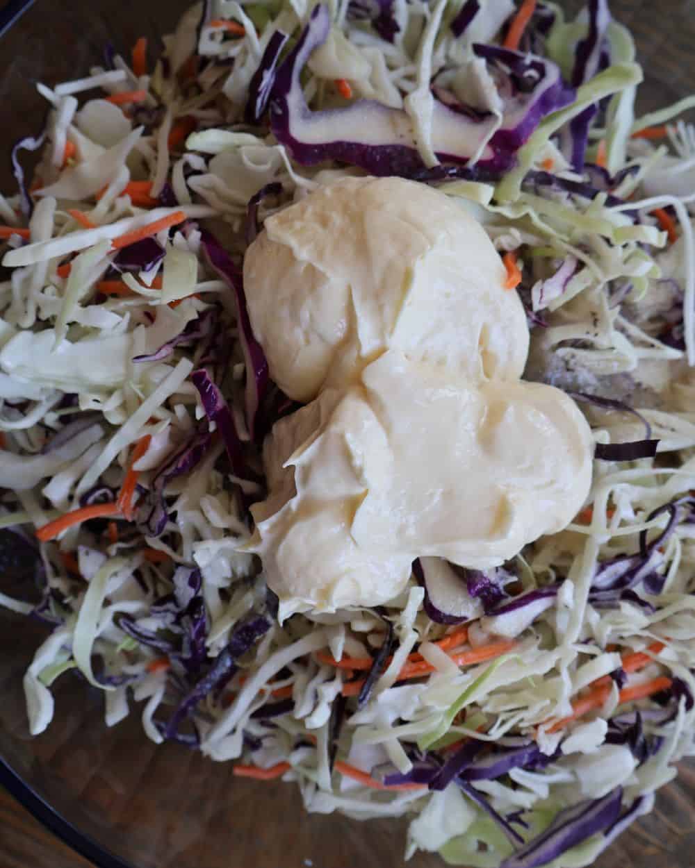 Mayonnaise dolloped over shredded cabbage and carrot in a glass mixing bowl