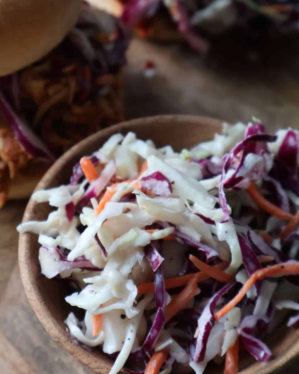 Finished creamy coleslaw in a wooden bowl next to a pulled pork sandwich