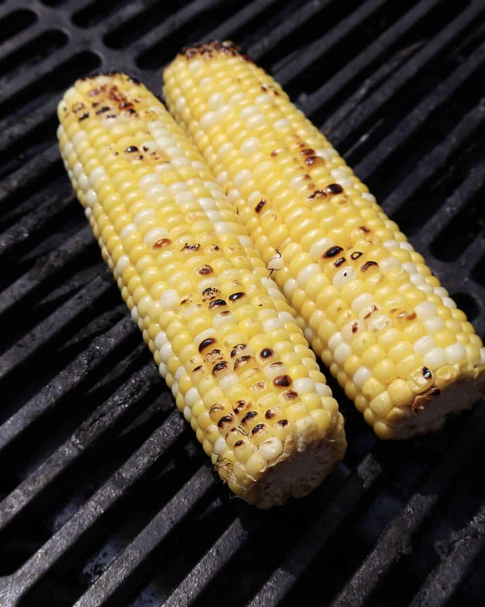 Two ears of corn charring on a grill