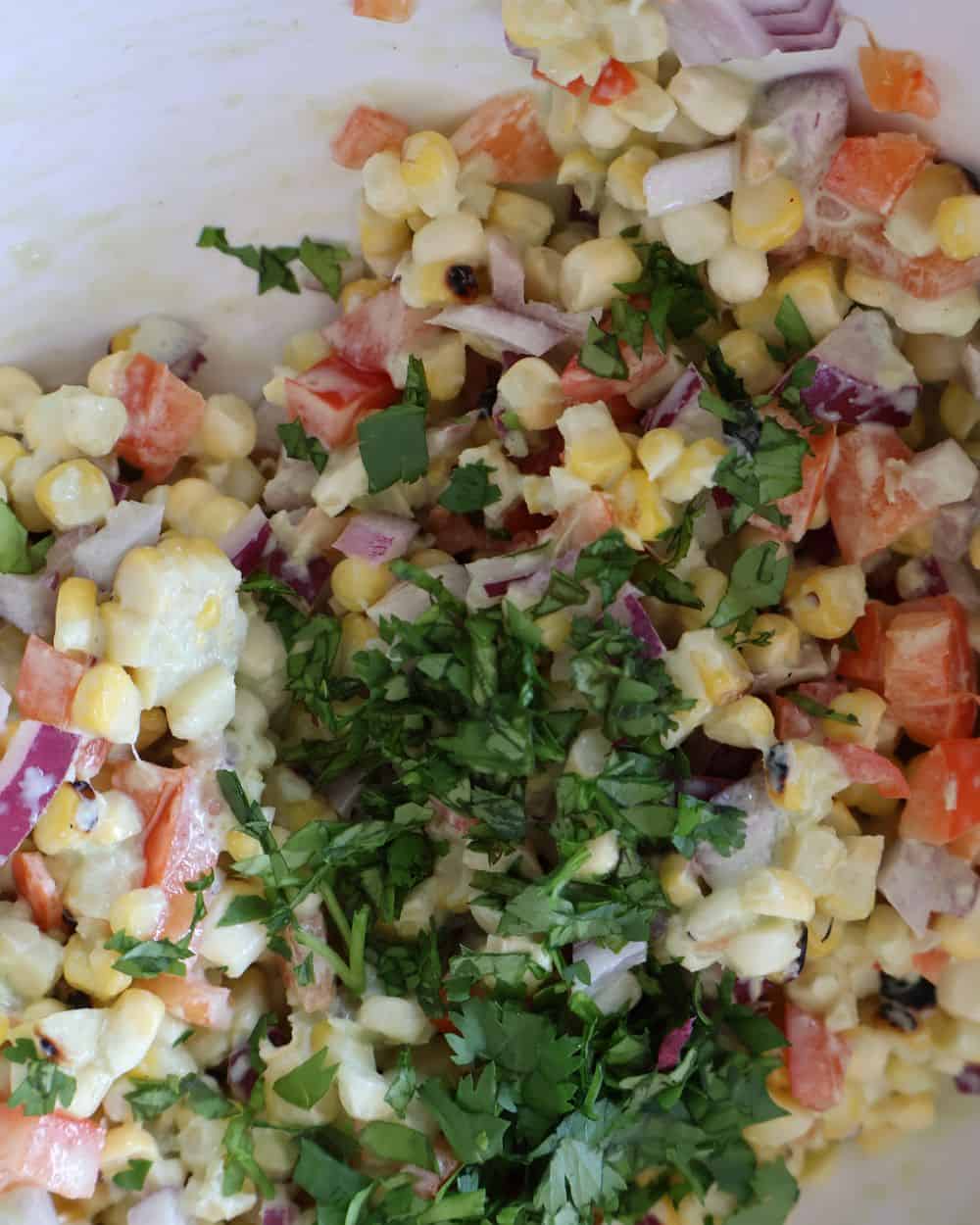 Corn kernels mixed with diced red pepper, red onion, and chopped cilantro in a bowl