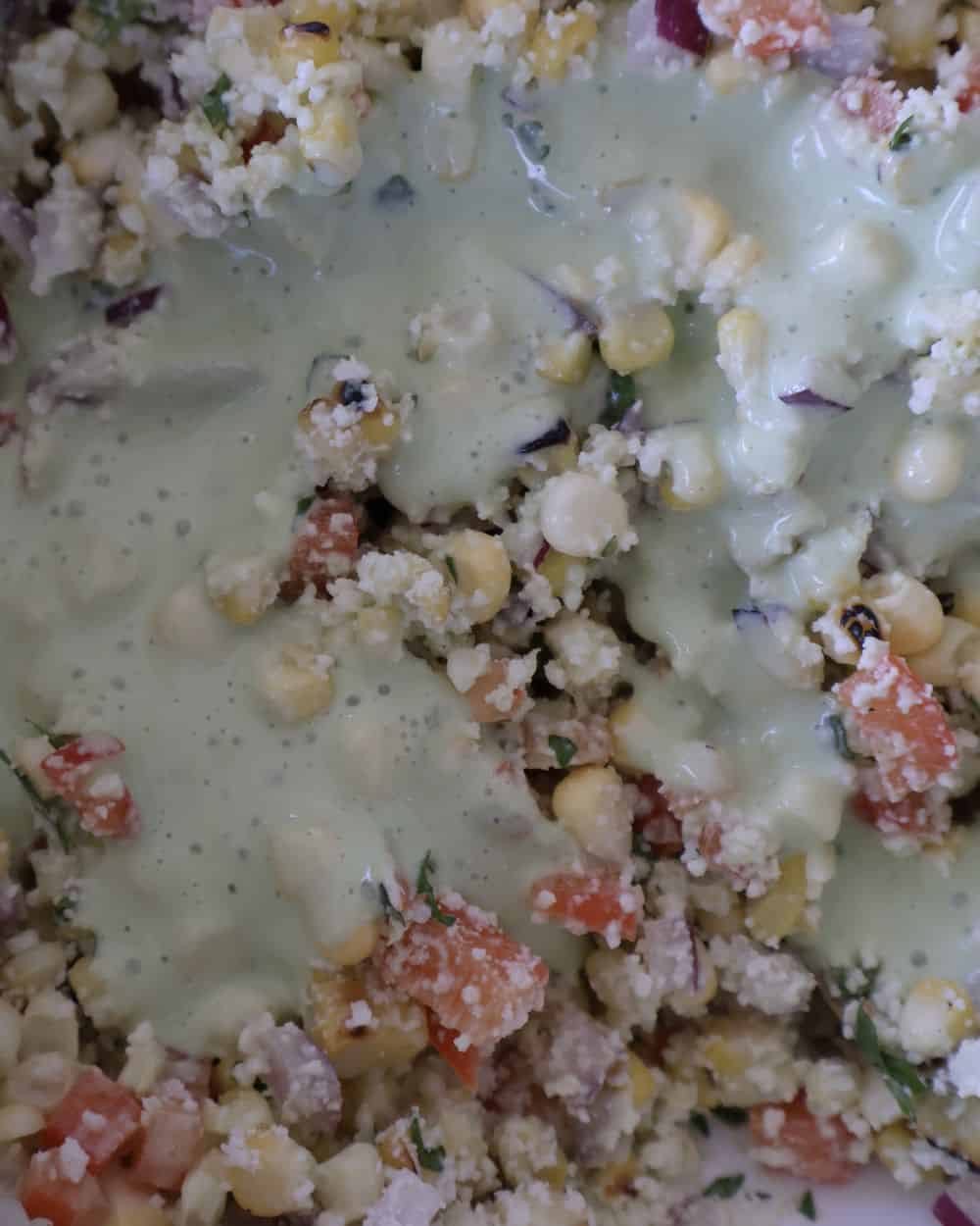 Cotija cheese and cilantro lime sauce being mixed into corn salsa