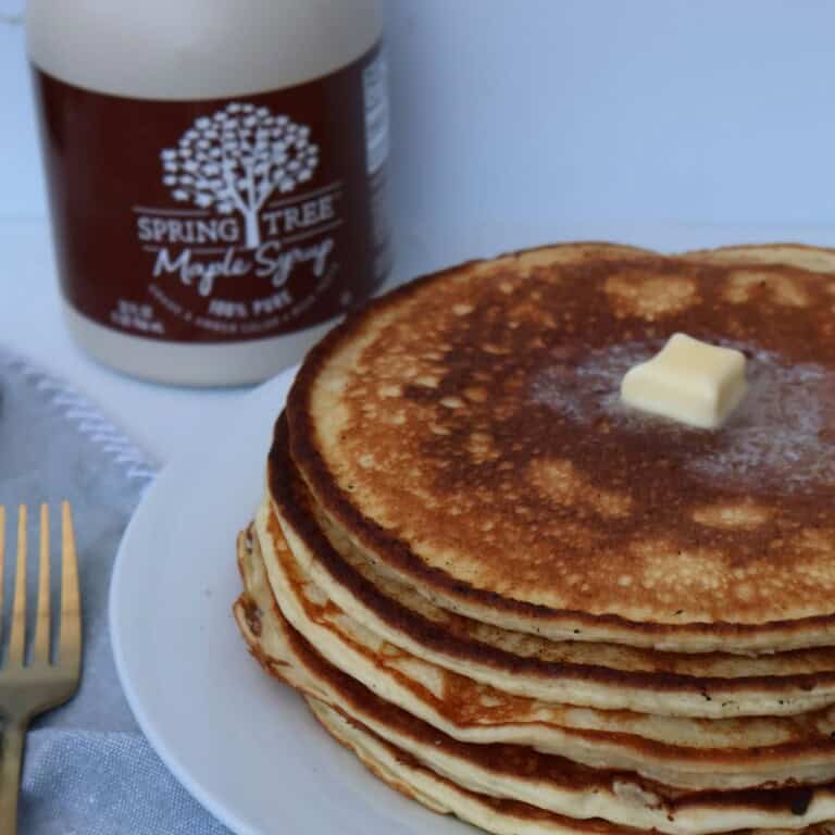 A stack of high protein cottage cheese pancakes on a white plate with butter melting on top