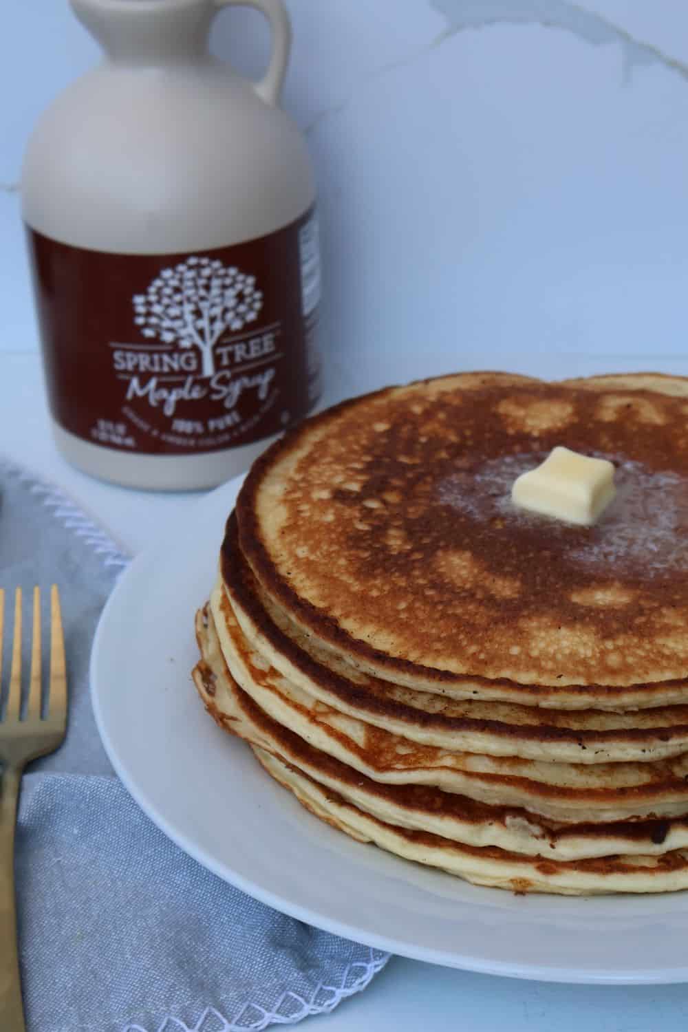 A stack of high protein cottage cheese pancakes with a pat of butter, next to a bottle of maple syrup