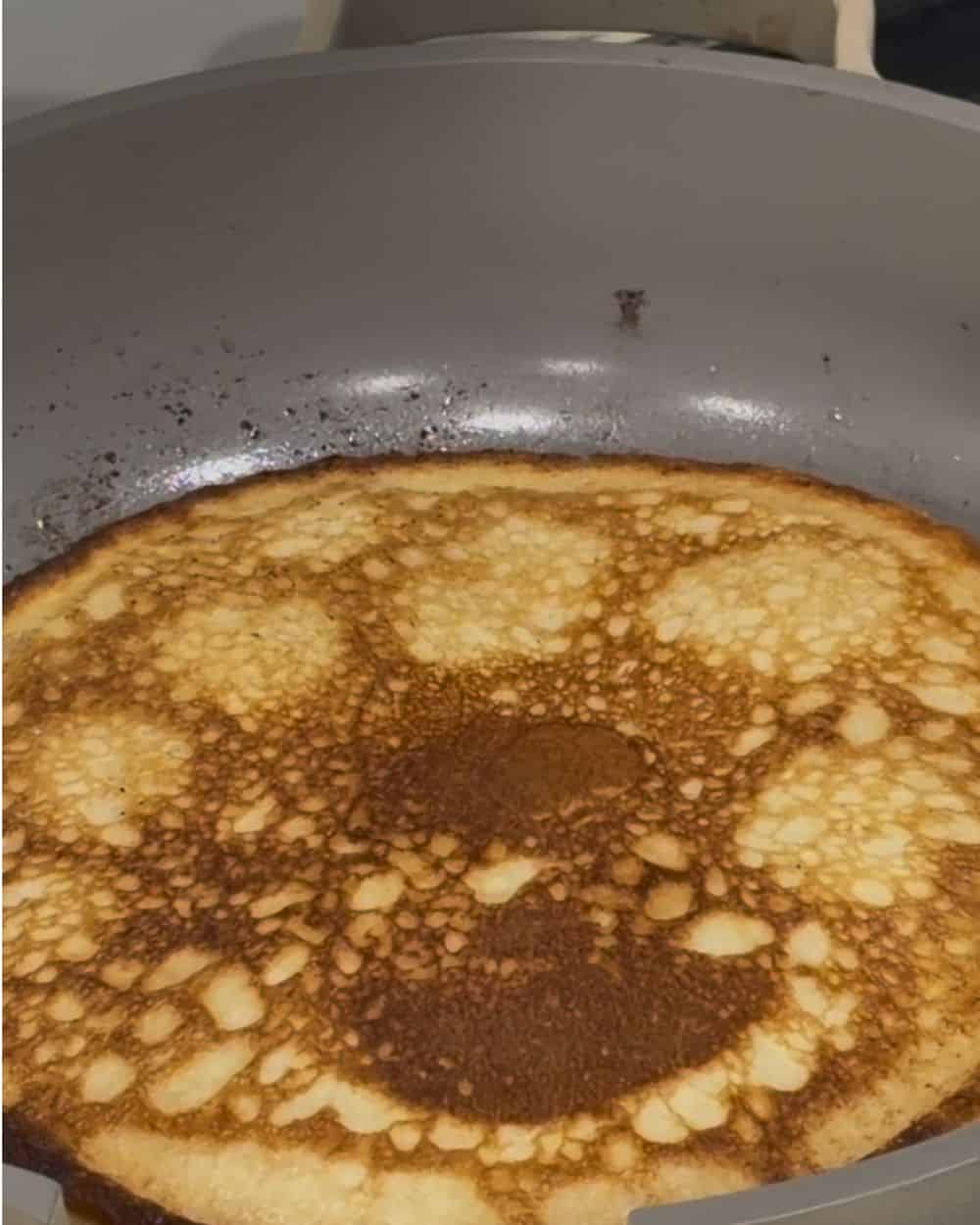 A cottage cheese pancake cooking in a skillet with bubbles opening across the surface