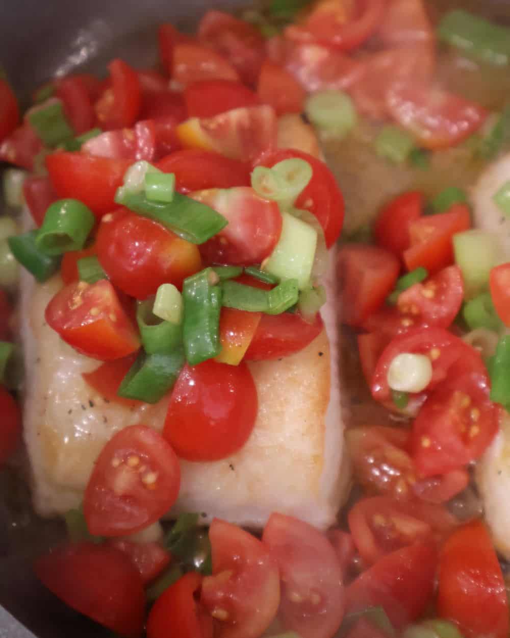 Seared sea bass in the skillet topped with tequila marinated tomatoes before going in the oven