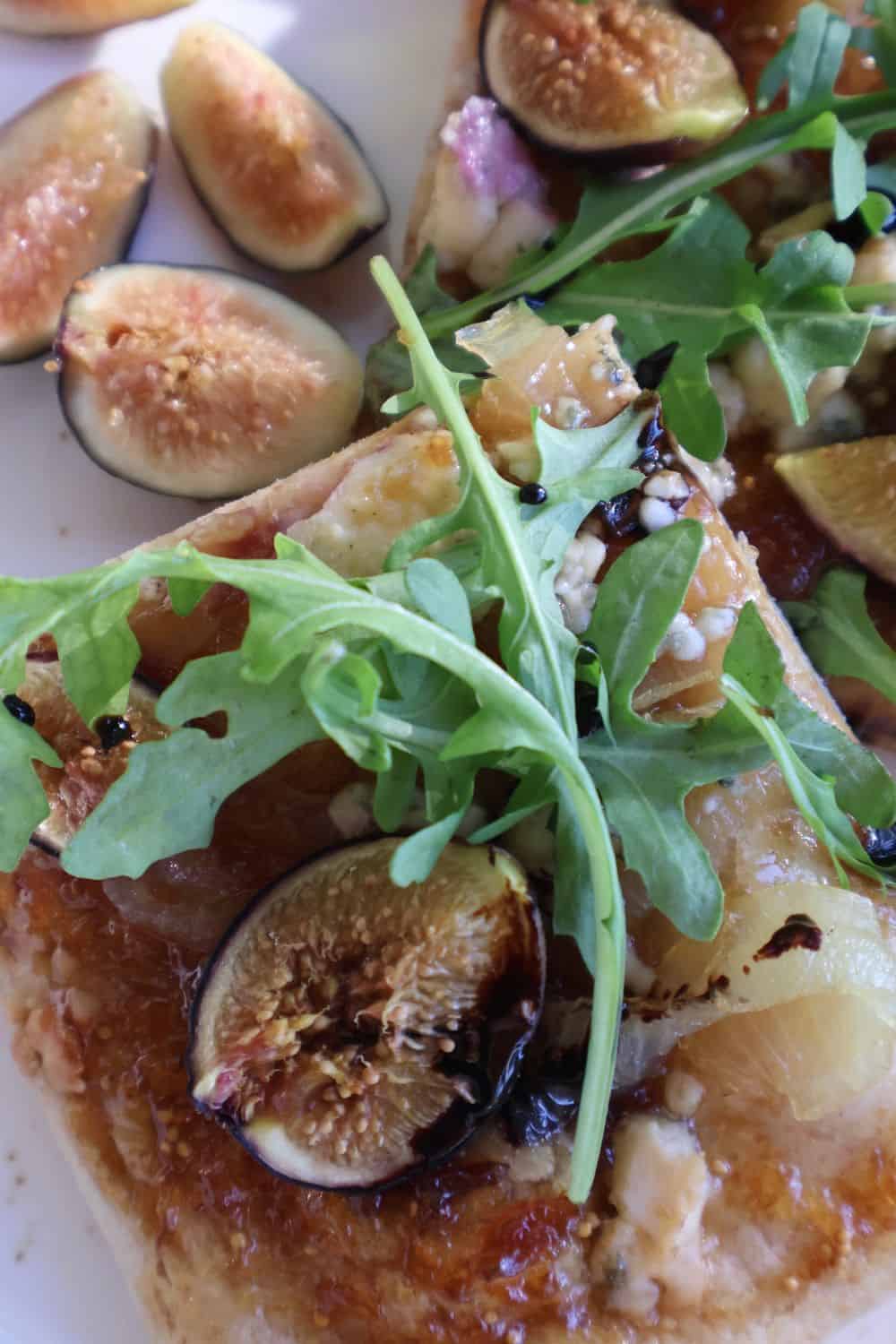 Fig gorgonzola flatbread topped with fresh figs, caramelized onion, arugula and balsamic drizzle, cut into pieces on a board
