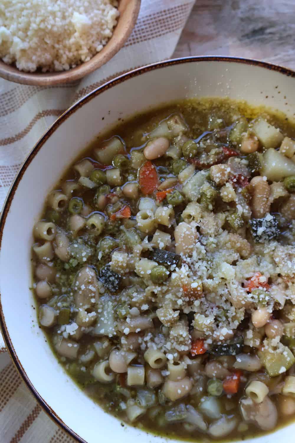 Pesto minestrone soup with white beans, ditalini and zucchini in a wide bowl, finished with olive oil and grated parmesan